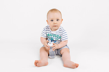 Fototapeta premium Smiling little child holding bottle with milk while sitting on white background