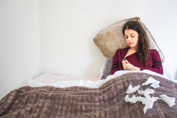 sick young woman with thermometer lying in bed