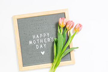 Minimalism style composition with text Happy Mother’s Day on the letterboard and bouquet of beautiful pink tulips on white background.