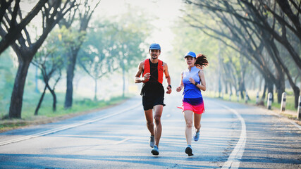 Full length of young couple in sport clothing running through the tree tunnel street together