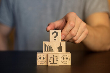 Business and finance concept. Hand holds wooden wooden blocks with finance icons and business. securities, student hat, 
books, time, home, car, family, question, target, gears,  securities, money, id