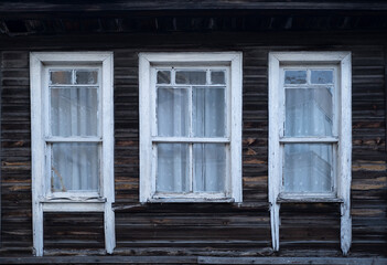 Three old wooden windows with white frames on a dark brown wooden wall of a country house