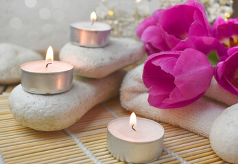 Close spa massage composition with pebbles, tulips, burning candles. Springtime wellness concept. Relaxation. Greeting card for Mothers day or wedding.
