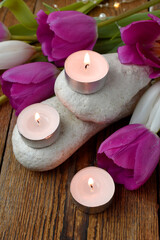 Close spa massage composition with pebbles, tulips, burning candles. Springtime wellness concept. Relaxation. Greeting card for Mothers day or wedding.