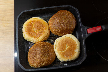 Burger bread with sesame is heating on a grill pan. Process of cooking self made burgers at home