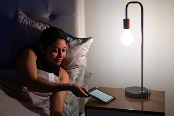 Night shot of a young woman in her bed. She has a electronic book reader in her hand