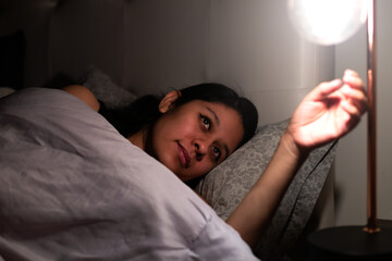 Night shot of a young woman in her bed. She is going to turn off her lamp to sleep