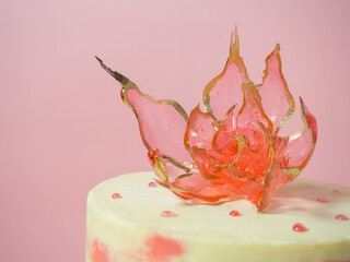 An edible red flower on top of an isomalt cake on a pink background