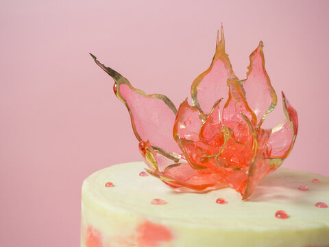 An edible red flower on top of an isomalt cake on a pink background