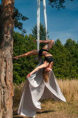 A slender girl with blonde hair, in a black stage costume, performs gymnastic and circus exercises...