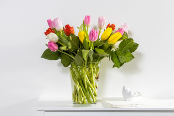 A bouquet of multi-colored tulips in a transparent vase and cup of tea