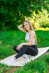 Beautiful blonde sits on the mat before training in the street. Athletic and healthy lifestyle