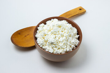 Cottage cheese on a white background. Homemade cottage cheese in a deep plate, next to a wooden spoon. Milk product