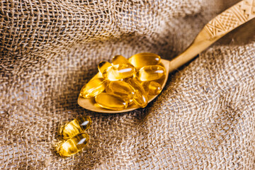 Fish oil capsules in a wooden spoon. Fish oil pills, tablets on the burlap. Vitamin complex omega...