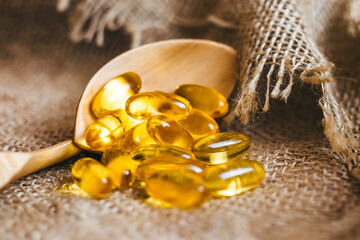 Fish oil capsules on a wooden spoon. Fish oil pills, tablets on the burlap. Vitamin complex omega...
