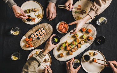 Japanisches Sushi-Abendessen für die Familie vom Lieferservice zu Hause. Flacher Tisch mit Lachs, Krabben, Garnelen, veganen Brötchen, Wasabi, Ingwer und Menschen, die zusammen auf dunklem Hintergrund essen, Draufsicht