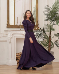 Beautiful pretty woman in long evening purple dress posing in luxury white interior. Elegant lady...