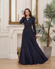 Beautiful pretty woman in long evening dark blue dress posing in luxury white interior. Elegant...