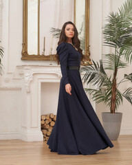 Beautiful pretty woman in long evening dark blue dress posing in luxury white interior. Elegant...