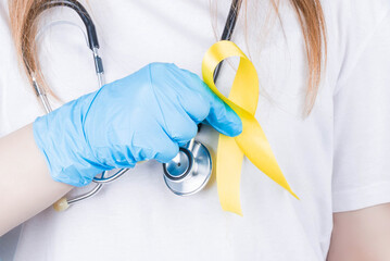 Female doctor holding yellow ribbon awareness symbol for suicide, sarcoma bone cancer, bladder...