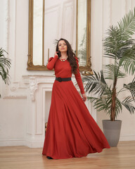 Beautiful pretty woman in long evening red dress posing in luxury white interior. Elegant lady with...