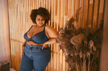 Beautiful stylish curvy oversize African black woman with afro hair posing in bra and jeans on...