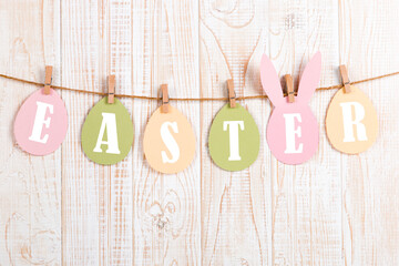 Inscription Easter on colored eggs, on a wooden background, a rope with clothespins. The concept of postcards for the Easter holiday.