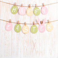 Inscription Happy Easter on colored eggs, on a wooden background, a rope with clothespins. The concept of postcards for the Easter holiday.