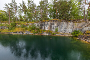 Obraz premium Beautiful nature landscape view of rain drops on pond surface. Ricky coast and tall pine trees on pale sky background. Sweden.