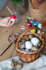 Easter composition on a wood table. Quail and chicken eggs in a basket. The woman paints Easter eggs on the background.