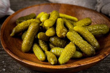 A bowl of pickled gherkins (cucumbers) on a rustic wooden background. Pickles