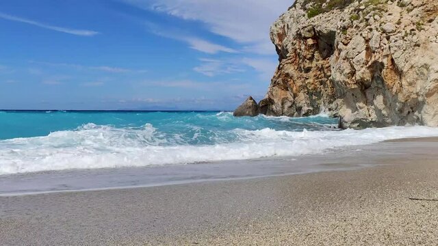 Azure bright vibrant stormy waves hitting rocky cliff on beach coast of Lefkada island in Greece. Summer wild nature travel to Ionian Sea