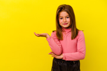 Little caucasian girl isolated on yellow background showing a copy space on a palm and holding...