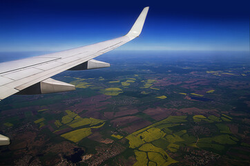 View from the airplane window of the wing and the landscape. View of fields, rivers and lakes from above