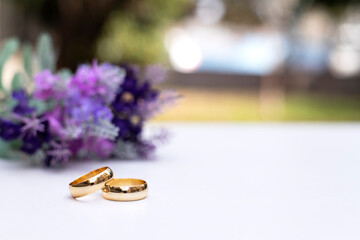 Purple flowers and two golden wedding rings on white table.