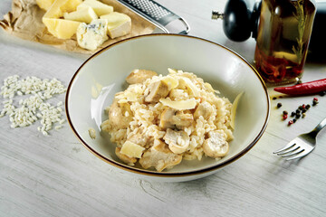 Classic Italian risotto with parmesan cheese, creamy sauce, chicken and mushrooms, served in a white bowl on a wooden background. Restaurant food