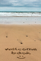 Fototapeta na wymiar Welcome back words written by hand on the sand of the beach. Holiday traveling vacation reopening concept.
