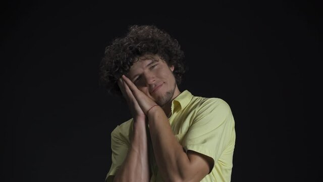 Tired and showing i want to sleep young guy with long curly hair isolated against a black background. 4K High definition footage. 