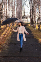 A young girl carefree walks with an umbrella in an autumn park on a sunny autumn day
