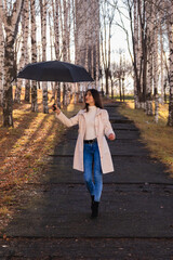 A young girl carefree walks with an umbrella along a path in an autumn park and enjoys a wonderful day