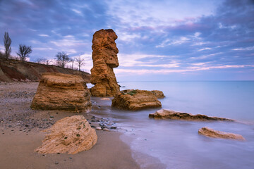 Beautiful seascape with shell rocks on the coast at sunset. One big stone like statue from Easter Island. Long exposure