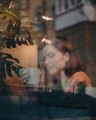 beautiful happy girl sits behind glass in a cafe. Rest by the window in the restaurant