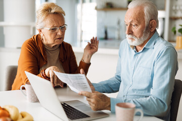 Frustrated senior couple sitting at home and checking their home finances