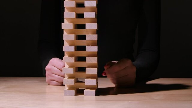 The girl plays the Jenga board game on a green gradient background. The tower of wooden blocks falls when the girl pulls out one of them. Camera movement from left to right. Slow motion. Close up.