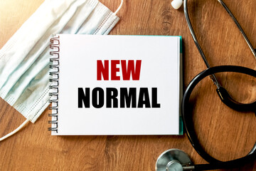 Inscription - NEW NORMAL. Written in a notepad to remind you of what's important. Top view of the table along with a stethoscope and a mask. Health care concept.