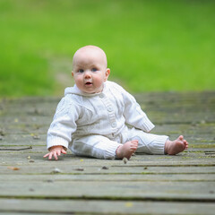 toddler in a white sweater sitting on a wooden bridge in the park