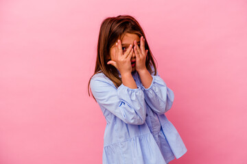 Little caucasian girl isolated on pink background  blink through fingers frightened and nervous.