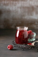 Raspberry jam in a glass jar with fresh raspberry berries on the old retro background.