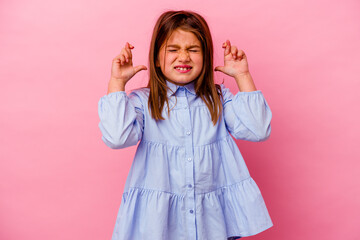 Little caucasian girl isolated on pink background  crossing fingers for having luck