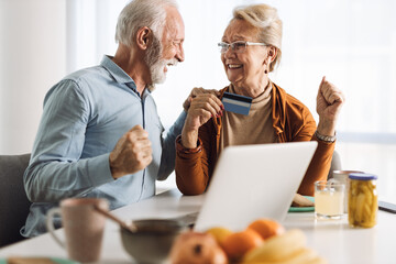 Cheerful senior couple using credit card for online shopping at home